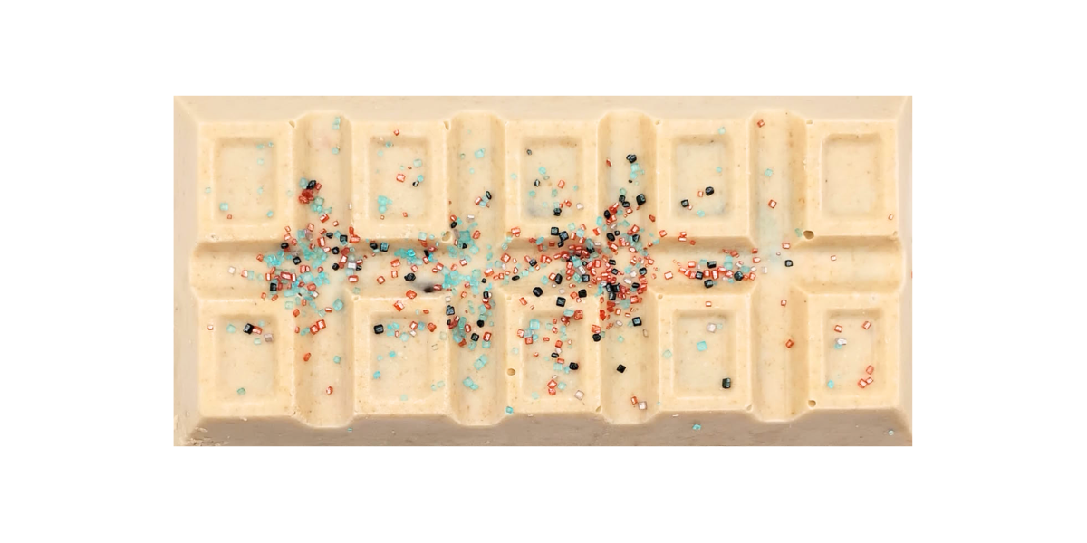 White chocolate bar with a smooth molded surface, topped with scattered blue, red, light blue, and dark blue sprinkles concentrated along the center.